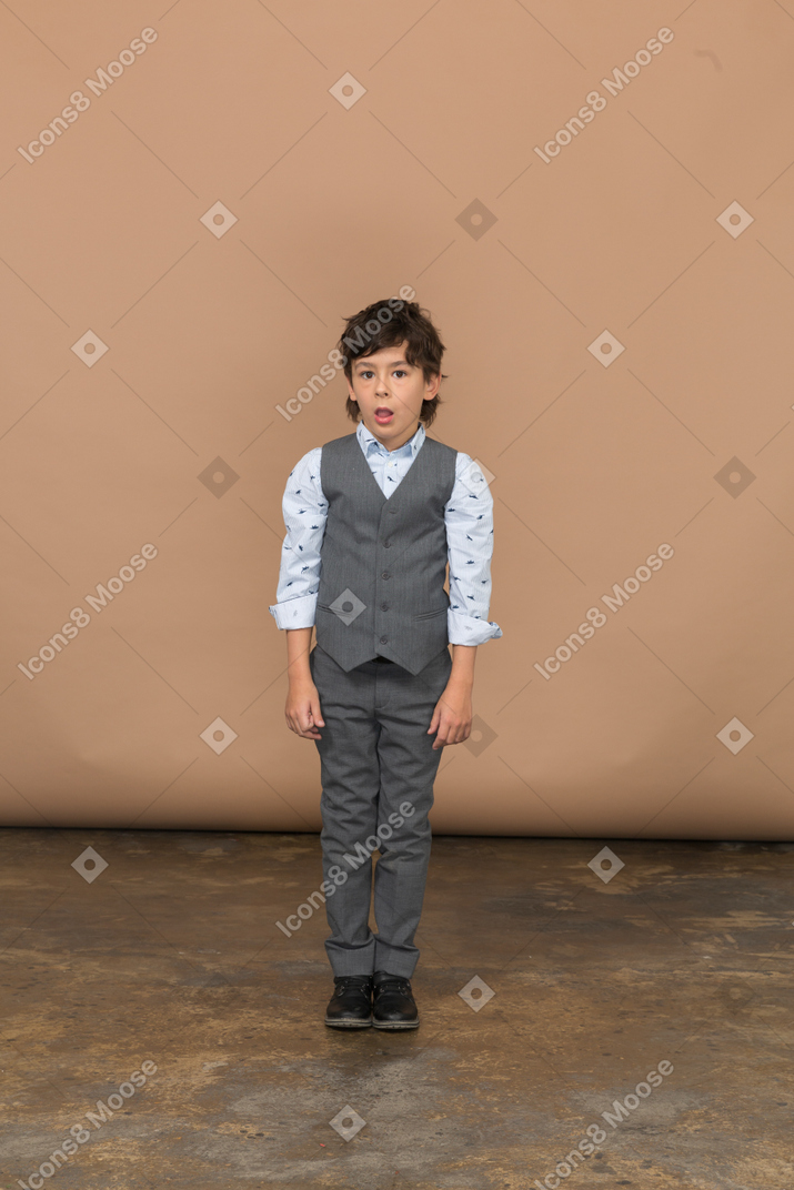 Vista frontal de um menino impressionado de terno cinza