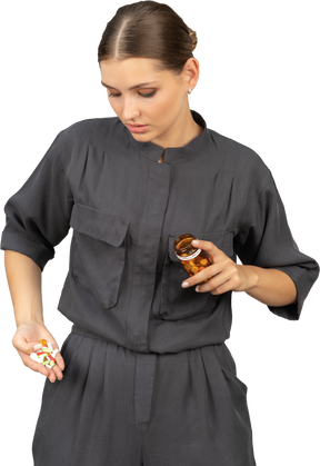 瓶から丸薬を見ているジャンプスーツの若い女性の正面図
