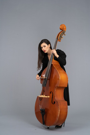 Three-quarter view of a young woman in black dress playing the double-bass with a bow