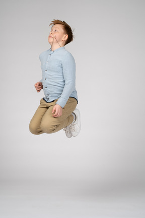 A boy in a blue shirt jumping with bent knees
