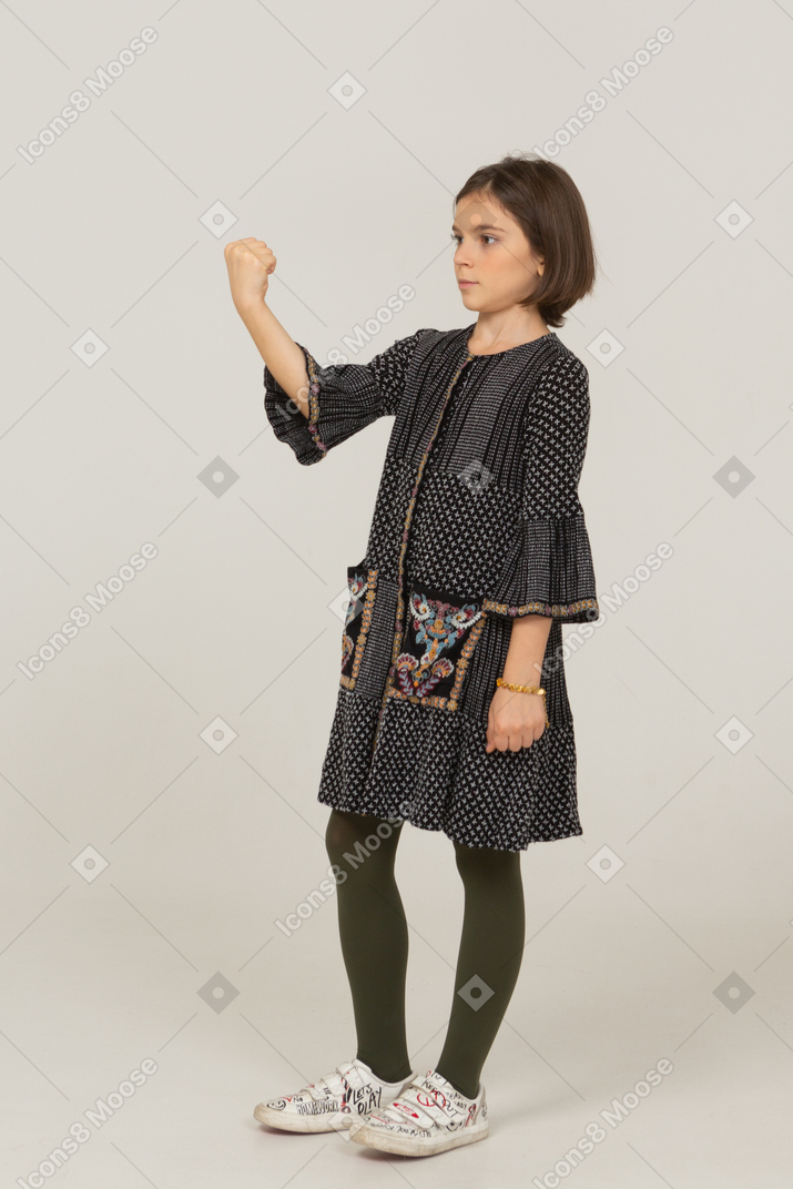 Vista de tres cuartos de una niña en vestido apretando el puño