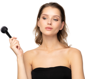Vista frontal de uma jovem pensativa e sensual segurando um pincel de maquiagem