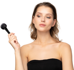 Front view of a thoughtful sensual young woman holding a make-up brush