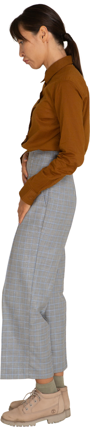 Vista lateral de uma jovem mulher asiática de calça e blusa tocando a barriga