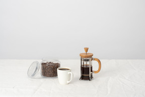 Coffee in french press, large cup of black coffee and jar with coffee beans