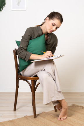 Vue de face d'une jeune femme réfléchie assise sur une chaise tout en passant un test papier