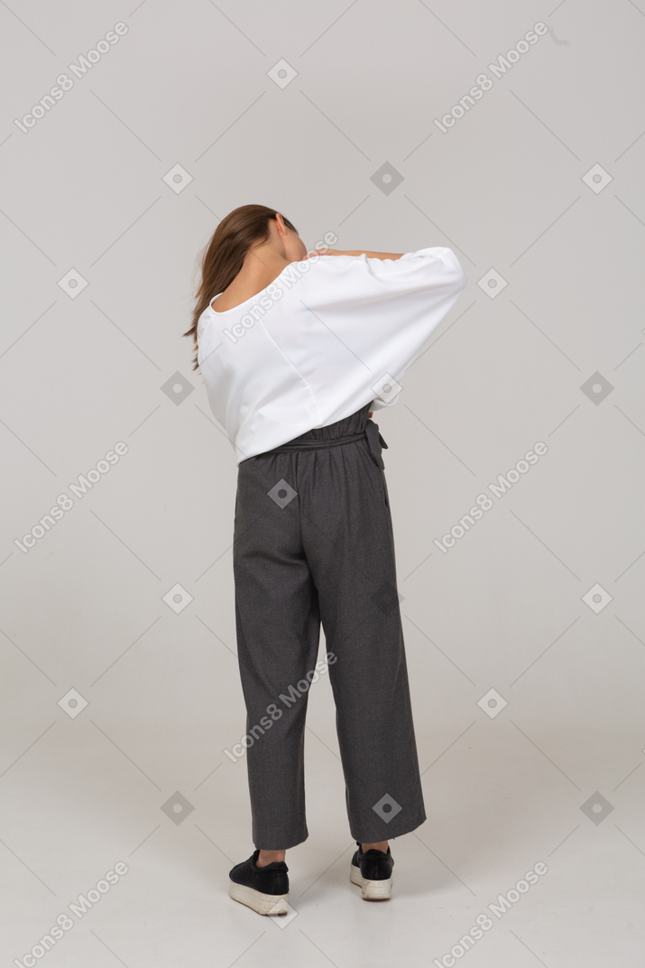 Vista posteriore di una giovane donna in abiti da ufficio che si aggiusta la camicetta