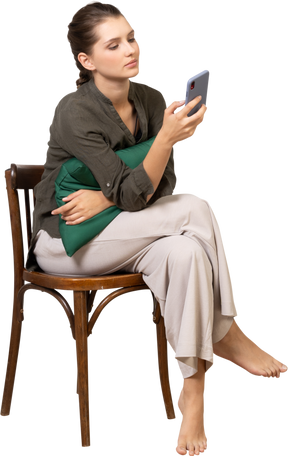 一个无聊的年轻女人坐在椅子上查看手机的正面视图
