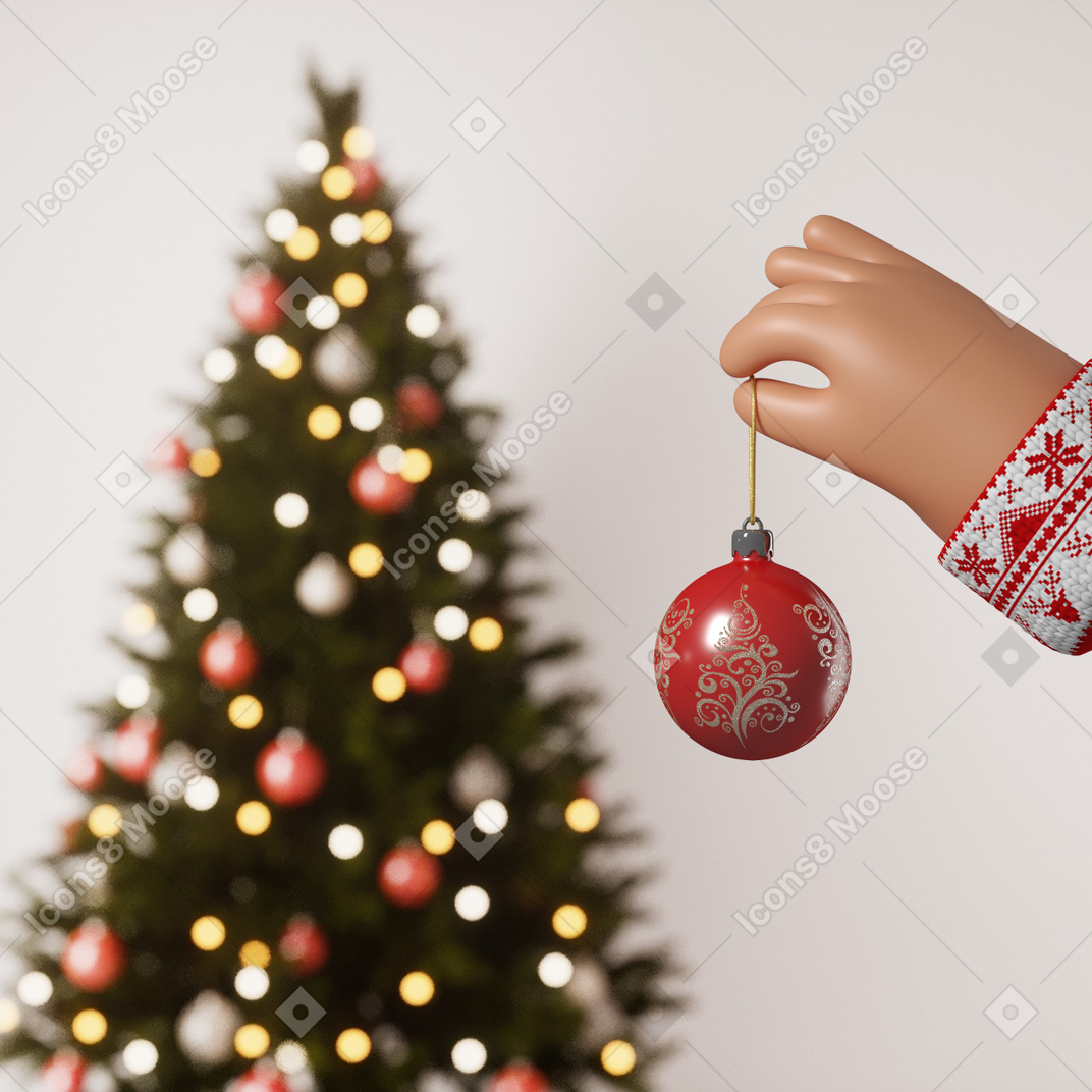 크리스마스 트리 근처에서 크리스마스 장식품을 들고 있는 손