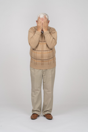 Vista frontal de un anciano con ropa informal que cubre la cara con las manos