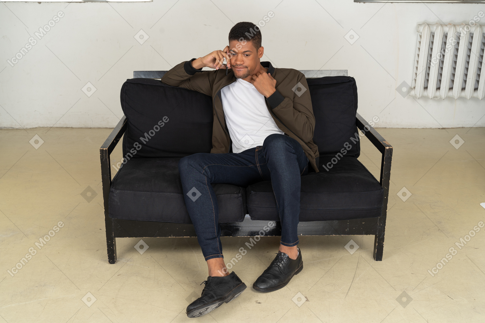 Front view of a perplexed young man sitting on a sofa