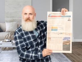 A bald man with a beard holding up a newspaper