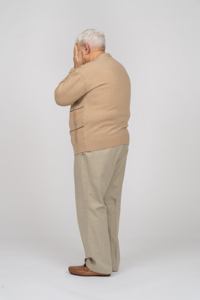 Vista laterale di un vecchio in abiti casual che coprono il viso con le mani