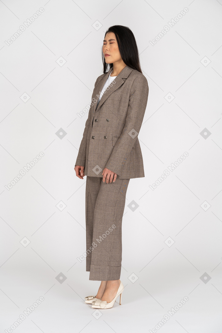 Вид в три четверти молодой леди в коричневом деловом костюме, закрывающей глаза