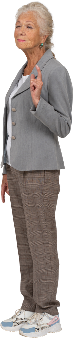 Vista lateral de una anciana en traje apuntando hacia arriba con un dedo