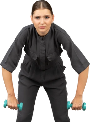 Front view of young woman in a jumpsuit doing exercises with dumbbells
