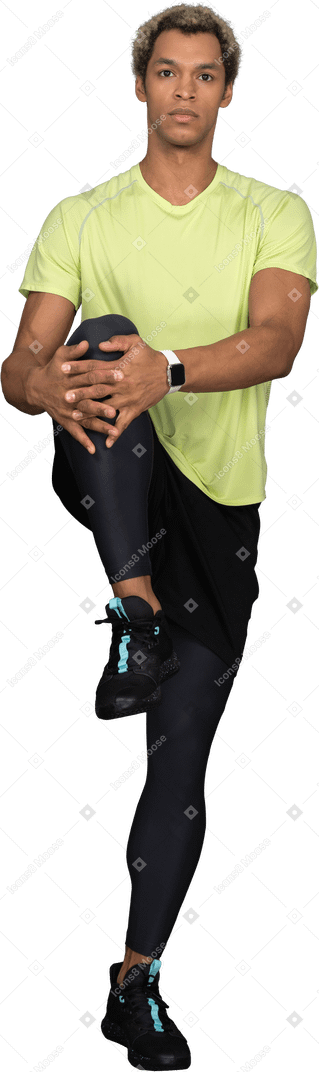 Vista frontal de un joven de piel oscura presionando la rodilla contra el pecho