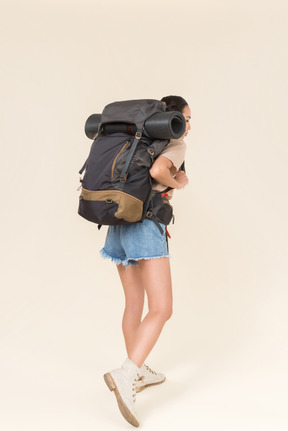 Young female hiker carrying heavy backpack and standing back to camera