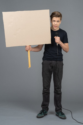Joven hablando por un micrófono y sosteniendo un cartel