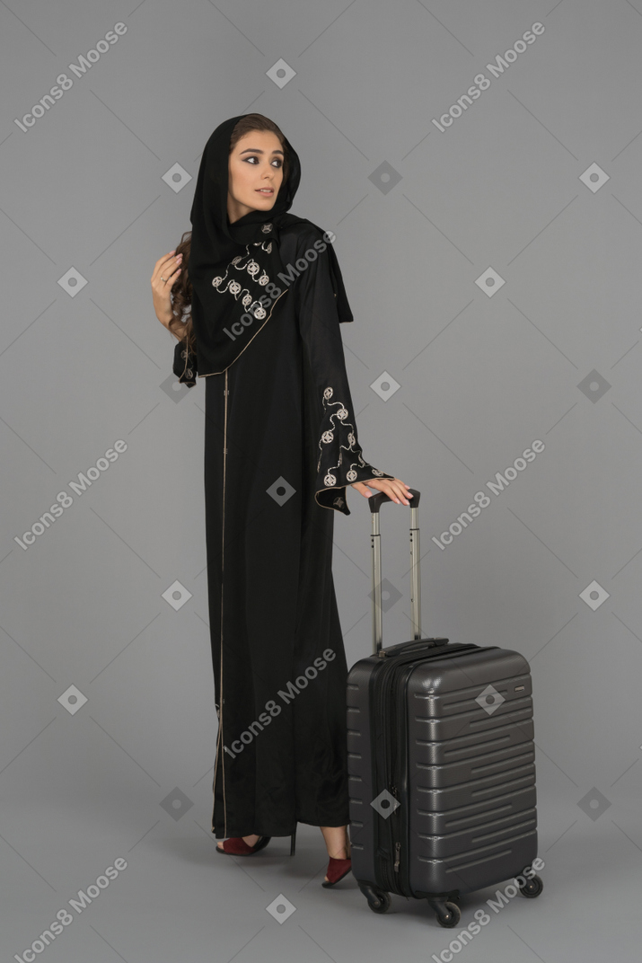 Una donna musulmana coperta in piedi con una borsa da viaggio