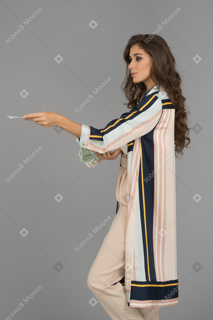 Beautiful young woman standing in profile with outstretched hand holding cash