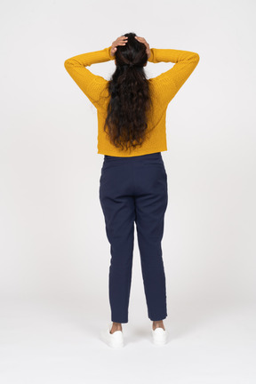 Rear view of a girl in casual clothes standing with hands on head