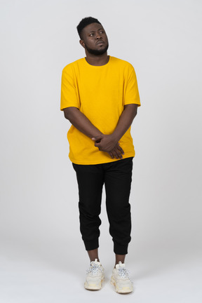 Front view of a shy young dark-skinned man in yellow t-shirt holding hands together