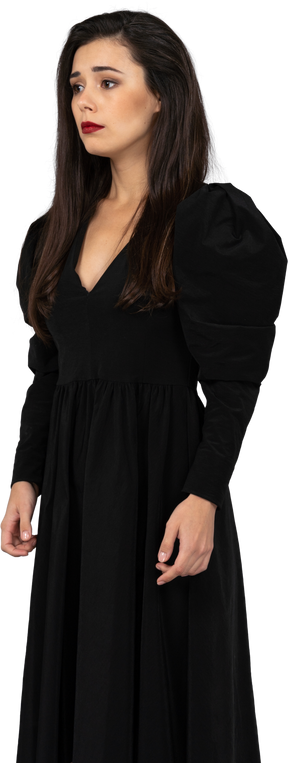 Трехчетвертный вид молодой девушки в черном платье, стоящей на месте