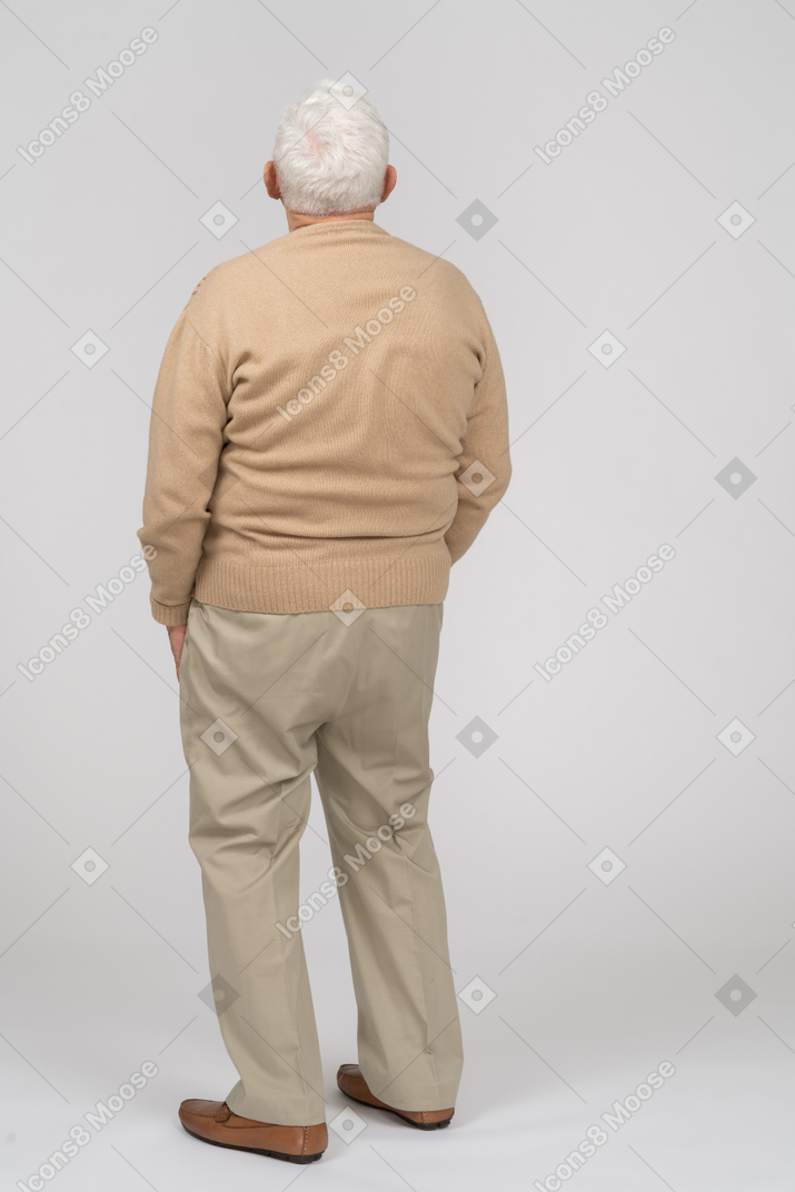 Rear view of an old man in casual clothes standing with hands in pockets and looking up