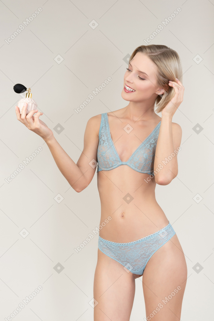 Sorrindo jovem em lingerie, olhando para atomizador de perfume