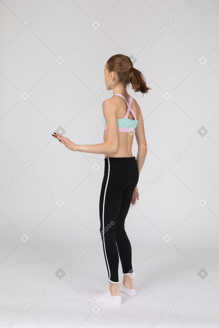 Три четверти сзади девушки-подростка в спортивной одежде, стоящей на месте и поднимающей руку