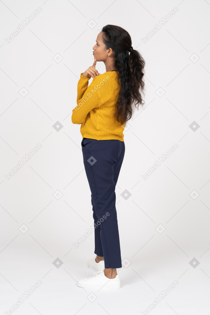 Vue latérale d'une fille réfléchie dans des vêtements décontractés touchant le menton avec les doigts