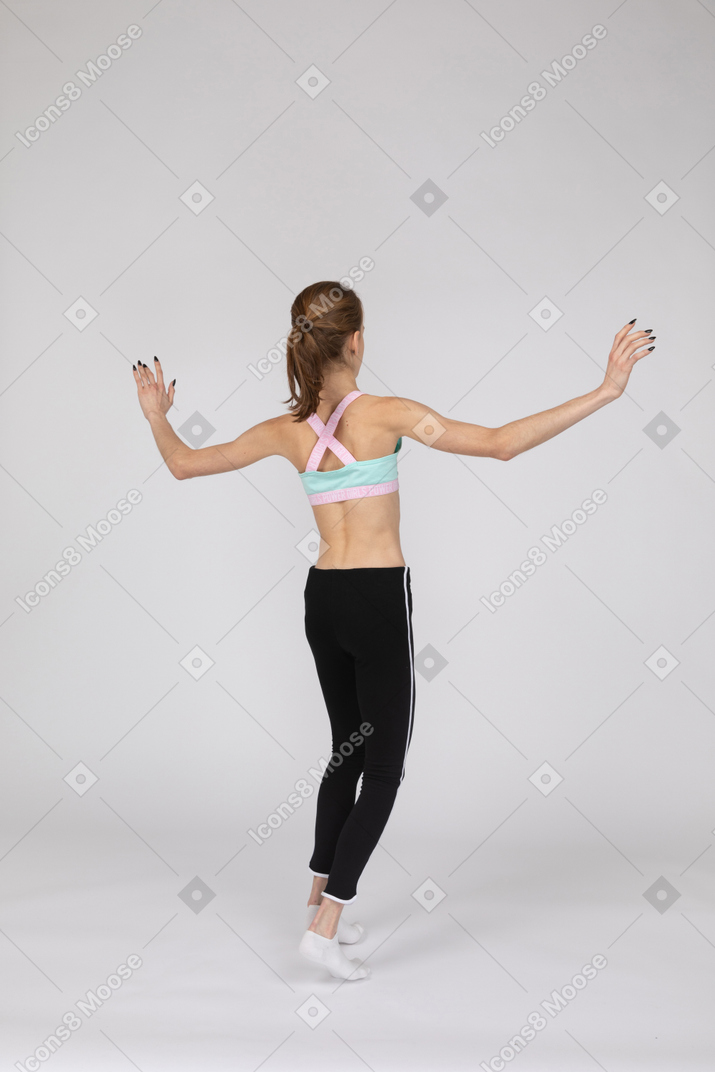손을 올리는 동안 발끝에 균형을 잡는 운동복에있는 십대 소녀의 3/4 다시보기