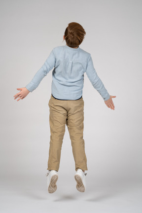Back view of a boy in a blue shirt jumping with his arms outstretched