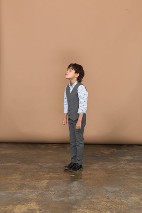 Vista lateral de um menino de terno cinza fazendo caretas