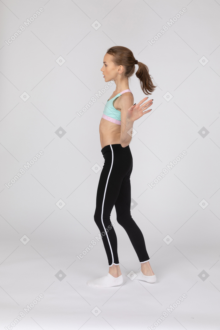 Vista lateral de uma adolescente em roupas esportivas, levantando as mãos e dançando
