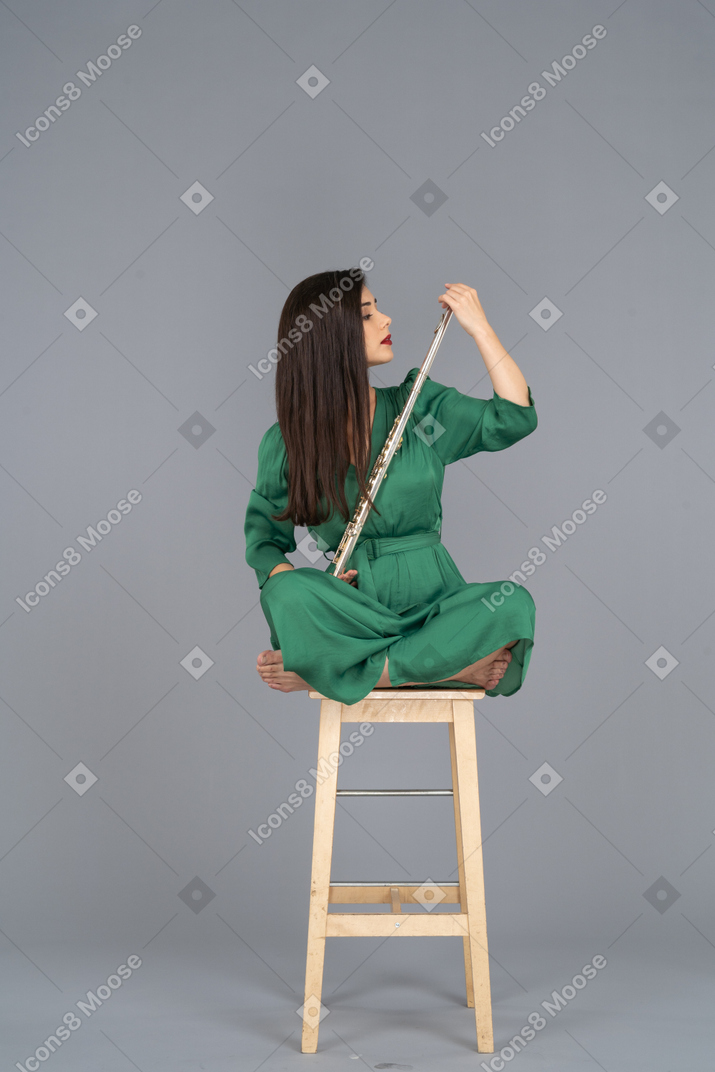 看着单簧管的年轻女士的全长，她的双腿交叉在木椅上