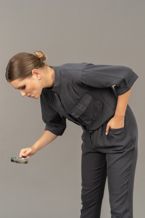 Three-quarter view of a young woman in a jumpsuit holding a magnifying glass