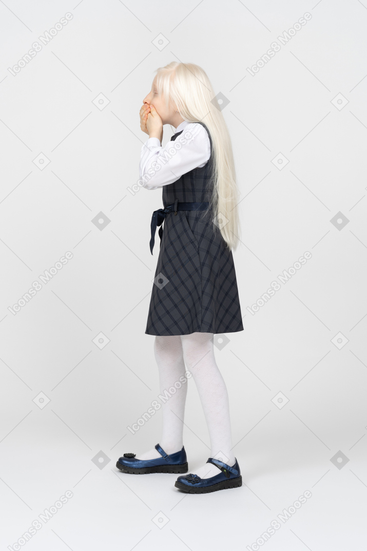 Side view of a schoolgirl covering mouth with hands