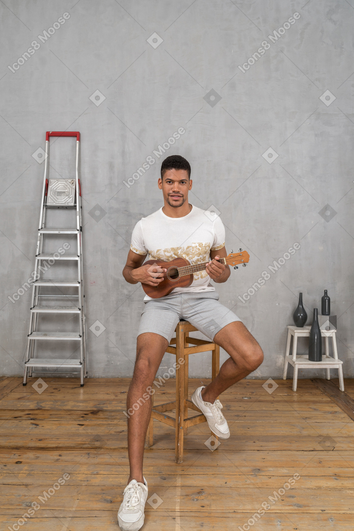 Front view of a man on a stool playing ukulele