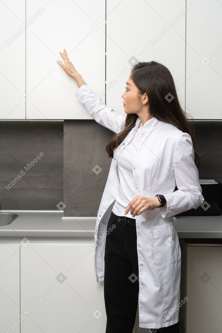 Three-quarter view of a young female doctor observing her medical cabinet