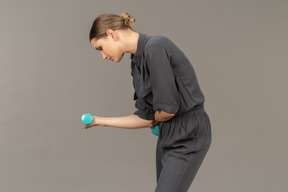 Side view of young woman in a jumpsuit doing exercises with dumbbells