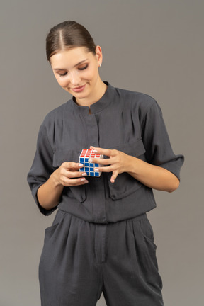 Вид спереди улыбающейся молодой женщины в комбинезоне, держащей кубик рубика