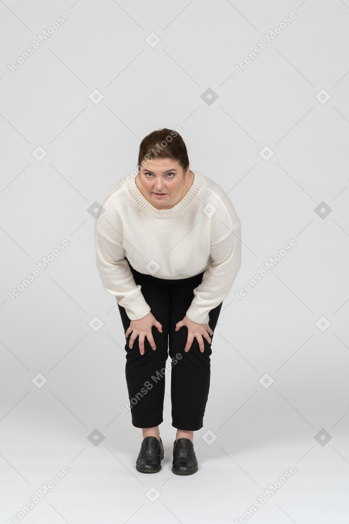Женщина больших размеров в белом свитере трогает больные колени