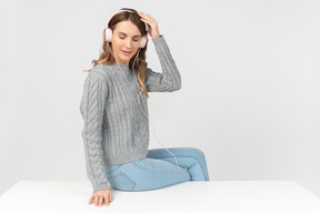 Young woman sitting on the table and listening music in headphones