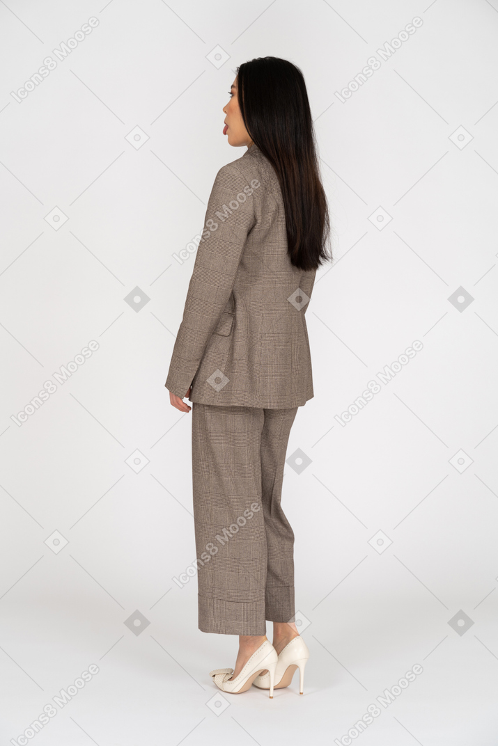 Vista posteriore di tre quarti di una giovane donna in tailleur marrone che mostra la lingua