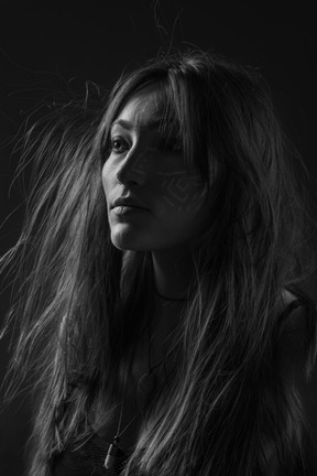 Noir three-quarter portrait of a young female with ethnic facial art and messy hair