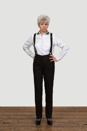 Full-length of an old  perplexed female in suspenders putting hands on hips