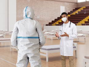 A man in a white lab coat talking to another man in a protective suit