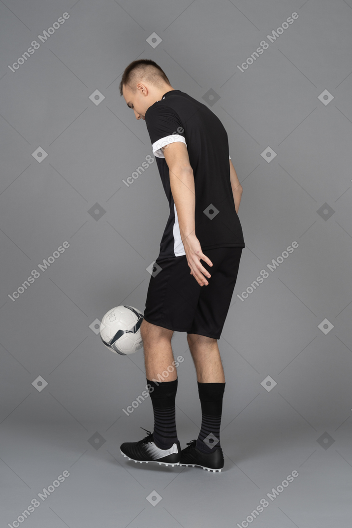 Vista traseira a três quartos de um jogador de futebol masculino com uma bola